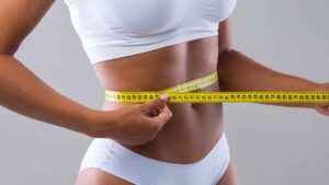 A close up of a fit model wrapping a measuring tape around her exposed abdomen in order to track her tone and fat reduction.