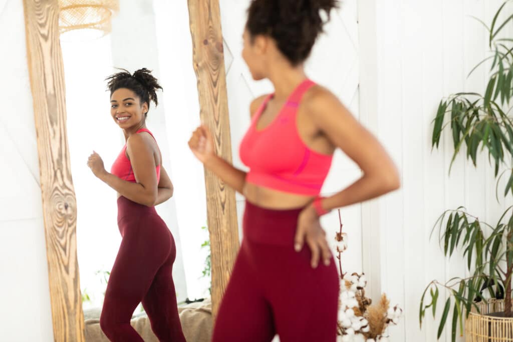 Woman looking joyfully in the mirror at her improved muscle tone and physique.