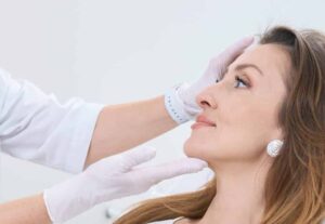 A gloved provider gently analyzing the face of a middle-aged woman.